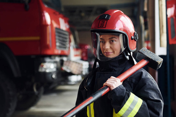 With hammer in hands. Female firefighter in protective uniform standing near truck. - Photo, image