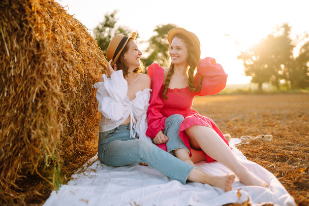 Two young women posing near haystack. Fashion concept. Nature, vacation, relax and lifestyle. Summer concept. - Photo, Image