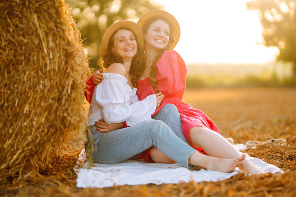 Two young women posing near haystack. Fashion concept. Nature, vacation, relax and lifestyle. Summer concept. - Foto, imagen