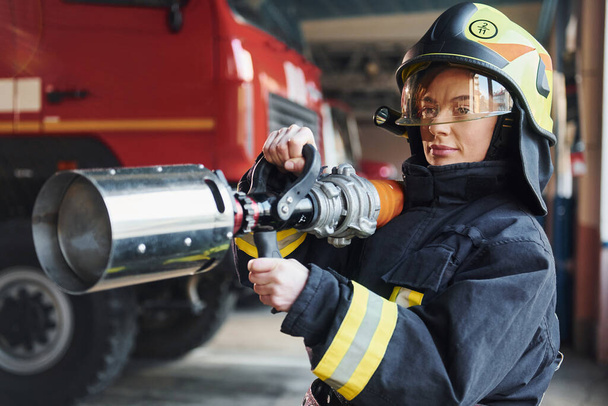 Hose in hands. Female firefighter in protective uniform standing near truck. - Fotografie, Obrázek