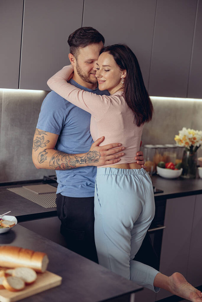 Happy young Caucasian man and woman smiling and hugging in kitchen. Romantic. - Photo, Image