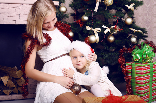tender photo of little girl with her pregnant mother beside a Christmas tree - Fotoğraf, Görsel