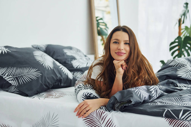 Front view of happy relaxed woman on bed. Interior and design of beautiful modern bedroom at daytime. - Valokuva, kuva