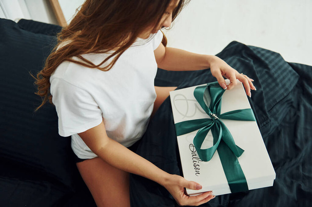 Gift box in hands of young woman. Interior and design of beautiful modern bedroom at daytime. - Valokuva, kuva