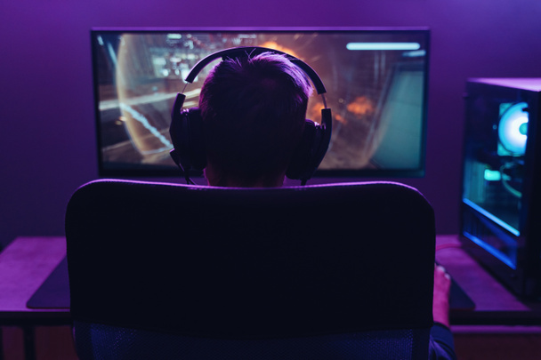 Guy pro gamer playing shooter video game in dark neon coloured room - Photo, Image