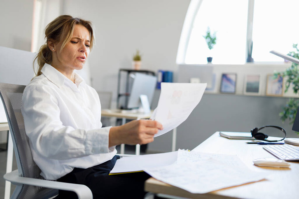 Επιχειρηματίας εξετάζει έγγραφα, ενώ κάθεται στο χώρο εργασίας γραφείο - Φωτογραφία, εικόνα