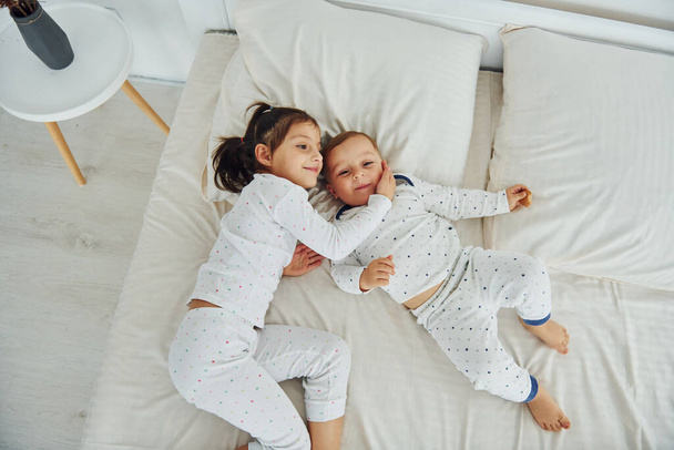 Two kids have fun while liyng down on bed. Interior and design of beautiful modern bedroom at daytime. - Valokuva, kuva