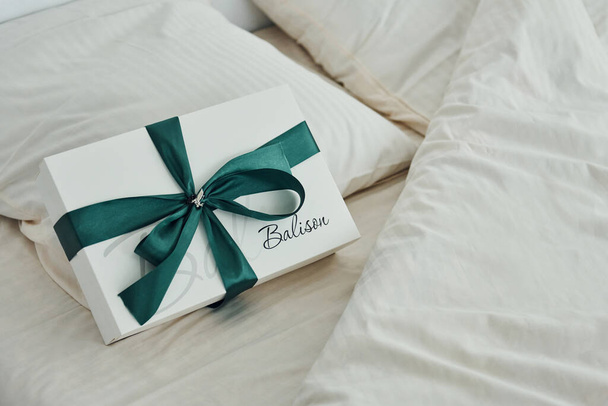 Подарочная коробка на белой кровати. Интерьер и дизайн красивой современной спальни в дневное время. - Фото, изображение