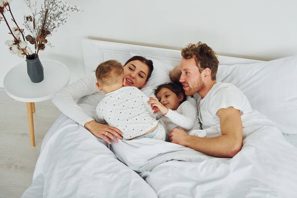 Nainen ja mies makaavat sängyllä lastensa kanssa. Sisustus ja suunnittelu kaunis moderni makuuhuone päivällä. - Valokuva, kuva