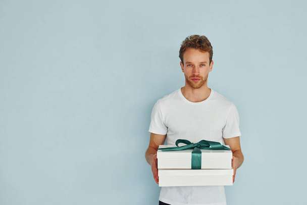 Молодий чоловік у білій сорочці стоїть на стіні і тримає подарункову коробку
. - Фото, зображення