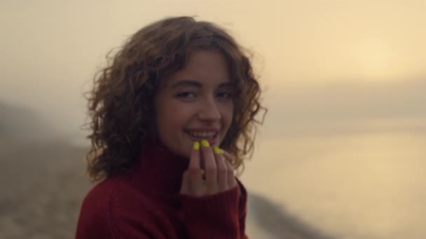 Fashionable woman smiling on camera. Happy girl posing at ocean beach at sunrise - Video