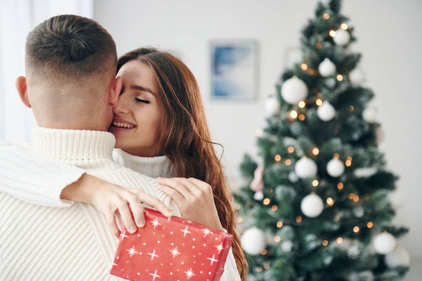 Girls holds red gift box. Young romantic couple celebrates New year together indoors. - Zdjęcie, obraz