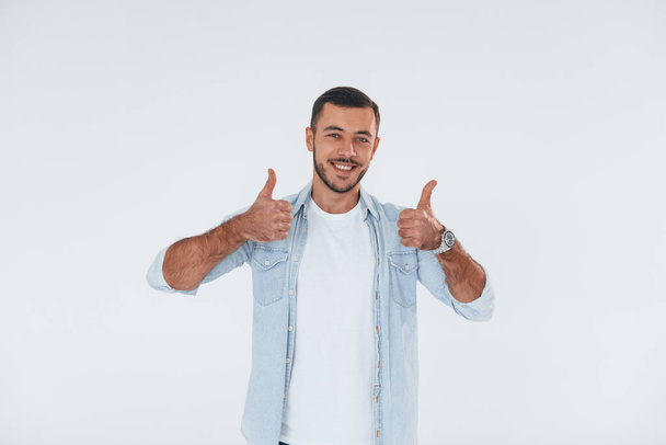 Thumbs up. Young handsome man standing indoors against white background. - Фото, зображення