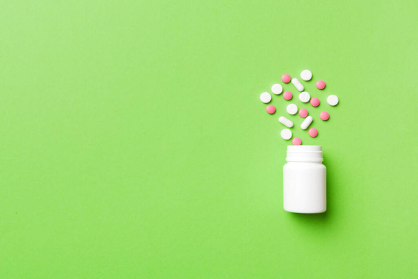 Bunte Pillen und Kapseln in Plastikflasche auf farbigem Hintergrund, Kopierraum. Viele verschiedene Medikamententabletten und Pillen, Vitamin- und Nahrungsergänzungsmittel. - Foto, Bild