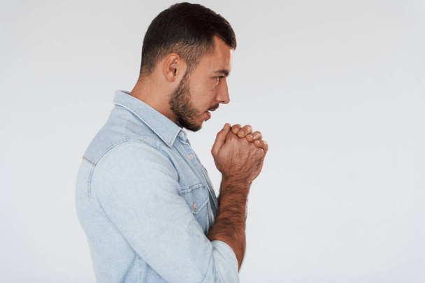 Guy is praying. Young handsome man standing indoors against white background. - Photo, image