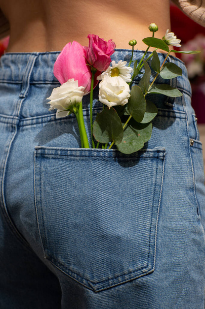 Woman with beautiful tender flowers in back pocket of jeans. Woman stabs back to camera. A tiny bouquet of field flowers in a back pocket of women's jeans. - Fotoğraf, Görsel