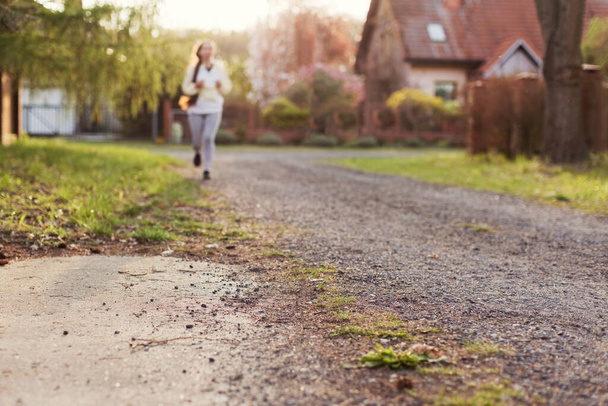 Correr mujer al aire libre a la luz del sol. Banner con calle del pueblo de verano con la mujer corriendo en el fondo - Foto, imagen