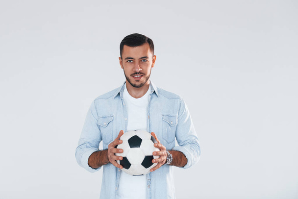 Football fan with soccer ball. Young handsome man standing indoors against white background. - Valokuva, kuva