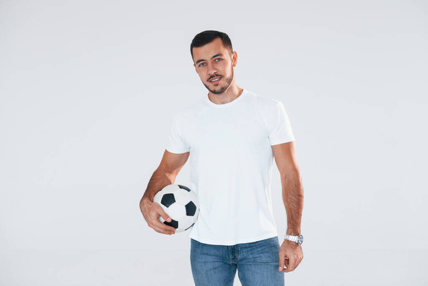 Football fan with soccer ball. Young handsome man standing indoors against white background. - Φωτογραφία, εικόνα