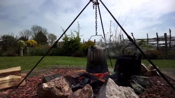 Eine alte Kaffeemaschine auf einem Stativ über dem Kochen des Lagerfeuers, auf dem feuerfesten Kopfsteinpflaster erhitzt sich das Teewasser in einer alten gusseisernen Kanne - Filmmaterial, Video