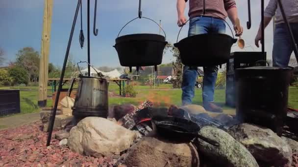 Zwei Freunde kochen am Lagerfeuer, kochen am knisternden Lagerfeuer, rühren in einer gusseisernen Pfanne um, gefilmt in 59,94 für Zeitlupe. Im Frühling im Garten - Filmmaterial, Video