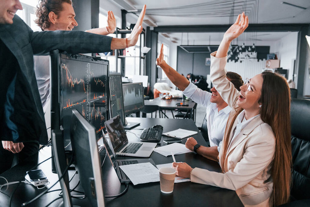 Giving high five. Team of stockbrokers works in modern office with many display screens. - Foto, Imagen