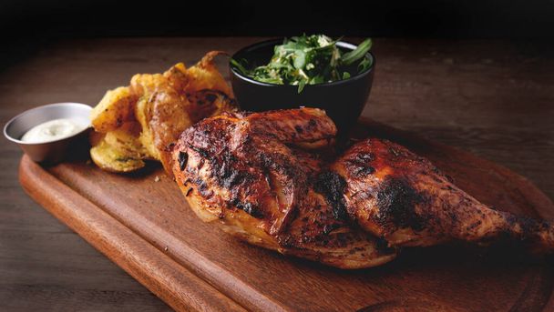 Peruvian food, Pollo a la brasa or grilled half chicken with fried yellow potatoes and arugula salad, wooden board. Selective focus - 写真・画像