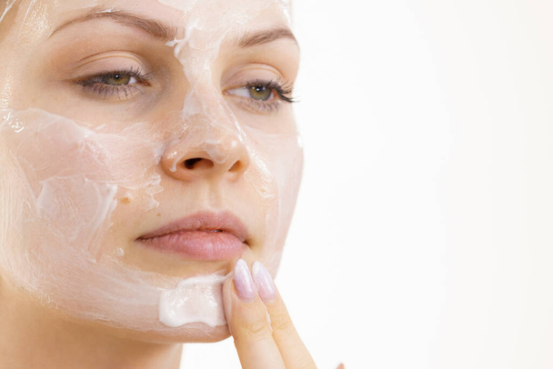 Young woman applying cream cosmetic, mask moisturizing to her face. Beauty treatment. Skincare. - Photo, image