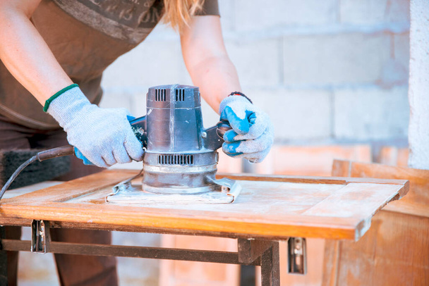 Tischlerin arbeitet mit Elektroschleifer-Werkzeug an Holzschrank. Frau Restaurierung und Reparatur alter Holzmöbel. Basteln zu Hause - Foto, Bild
