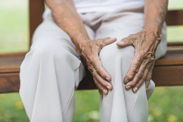 Senior woman sitting on bench, holding her painful knee - Фото, зображення