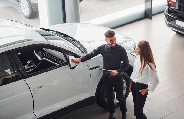 Woman choosing car by help of male assistant indoors in the salon. - 写真・画像