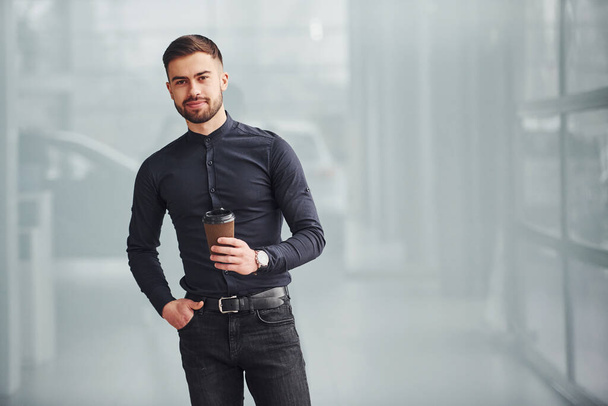 Young bearded guy in elegant clothes standing indoors against grey background. - Valokuva, kuva