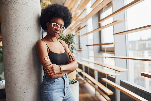 African girl with curly black hair and in casual clothes standing indoors. - Foto, Bild