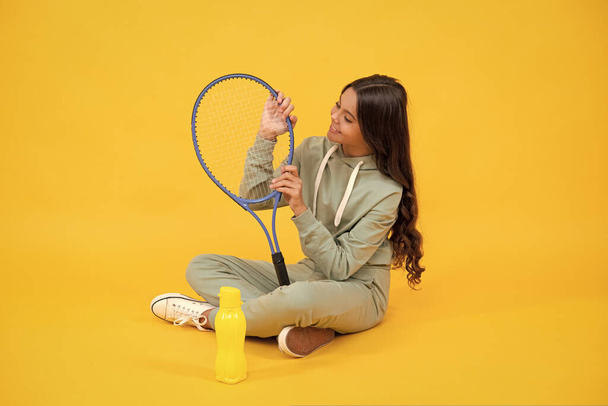 Счастливого детства. обезвоживание. ребенок сидит с ракеткой и бутылкой воды. ребенок с теннисной ракеткой - Фото, изображение
