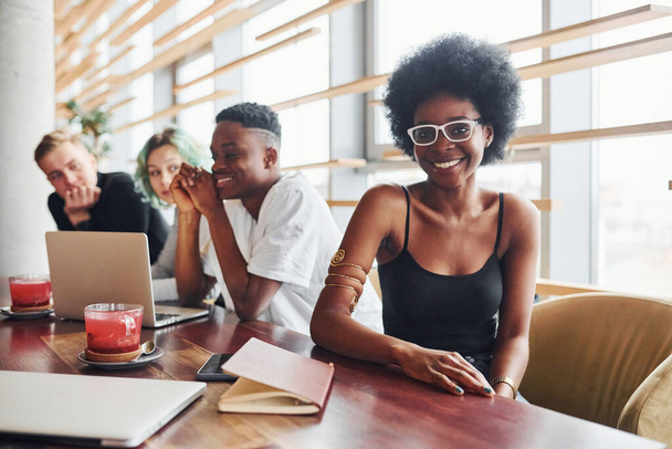 Black woman sitting in front of group of multi ethnic people with alternative girl with green hair is working together by the table indoors. - Foto, Imagem