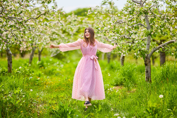 a young woman in a pink dress posing next to a blossoming apple, spring portrait. - Foto, immagini