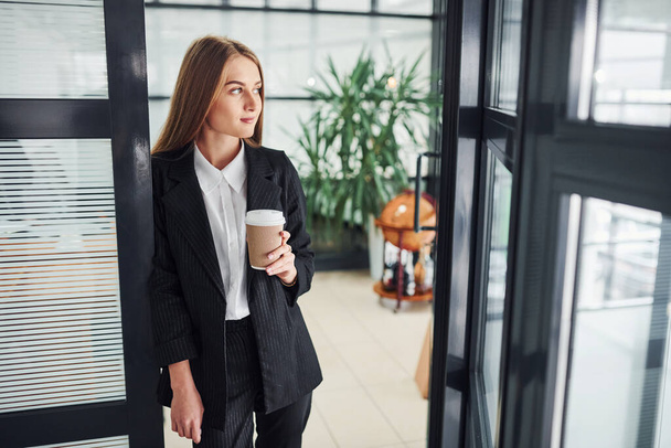 Woman in formal clothes standing indoors in the office with cup of drink. - Foto, Bild