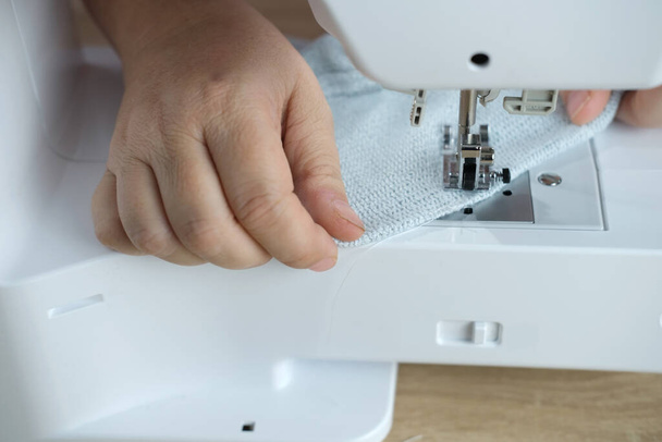 close-up of female hands perform work on a white sewing electric computer machine, stitches appear step by step on the fabric, concept of tailoring, women's hobby, modern needlework - Fotoğraf, Görsel