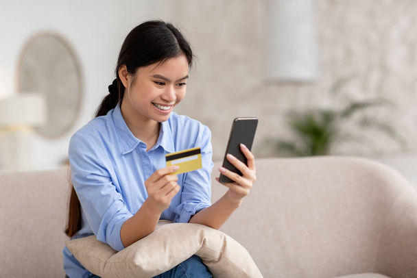 Positive asian woman shopping online, using smartphone and credit card - Foto, Imagen