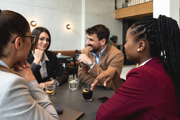 Group of modern intercultural brokers in smart casualwear sitting by table, having coffee, brainstorming and discussing new strategies at meeting. Young freelancers business people in the coffee shop. - Foto, Imagem