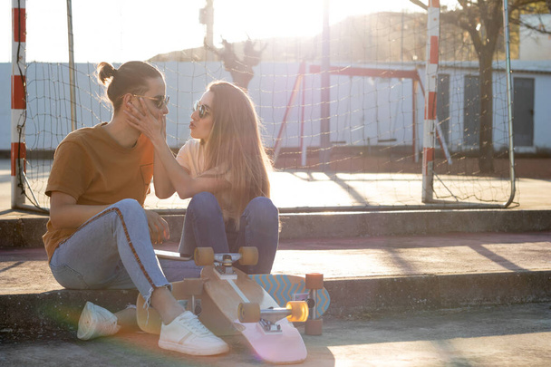 Linda pareja adolescente joven divirtiéndose y bromeando con skate board alrededor al atardecer con bengalas alrededor - Foto, Imagen