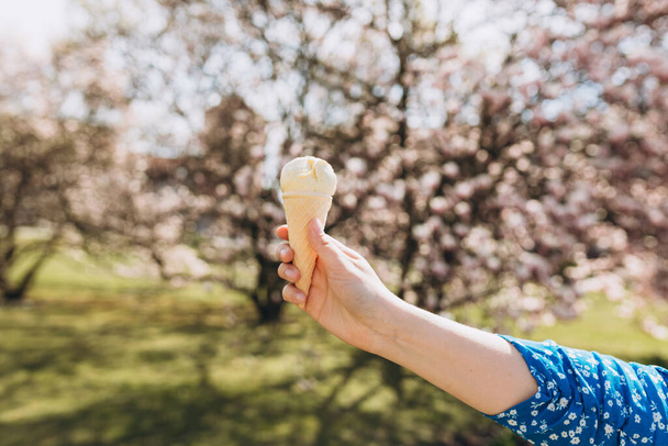 Close up womans hand with delicious white ice cream in waffle cone outdoors. Spring time, food banner - Foto, Bild