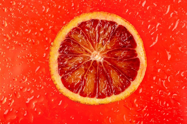 Секция спелого сицилийского апельсина на красном фоне с каплями - Фото, изображение
