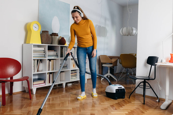 full length body shoot of woman vacuuming floor at her home - Photo, Image