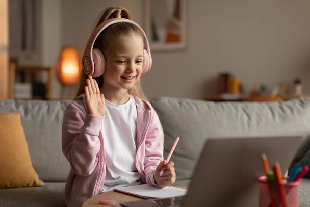 Kleines Schulmädchen winkt Laptop-Lernen zu Hause zu - Foto, Bild