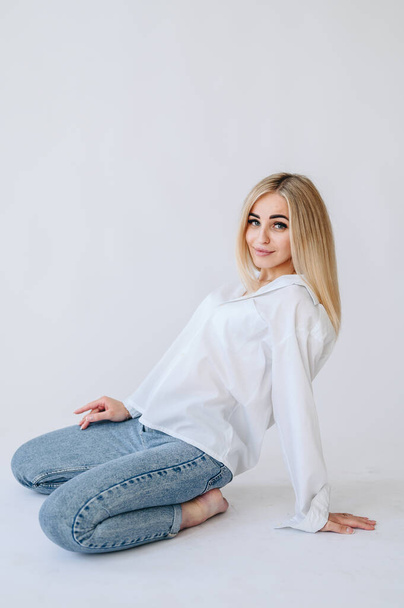 A girl in jeans and a white shirt leaned on her arm from behind. Girl on a white background in jeans. - Photo, Image