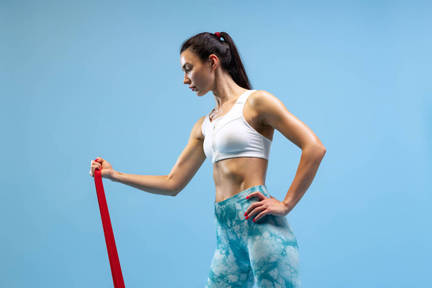 Half-length portrait of young sportive woman training, doing exercises isolated over blue studio background - Foto, Imagem