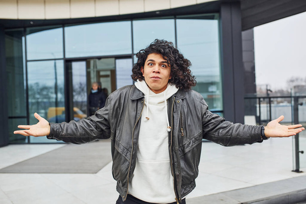 Handsome young man with curly black hair posing for the camera on the street against building. - Foto, Bild