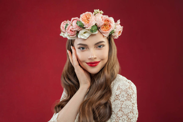 Mooie vrouw met zomerrozenkrans portret. Glimlachend model met bloemen op rode achtergrond - Foto, afbeelding