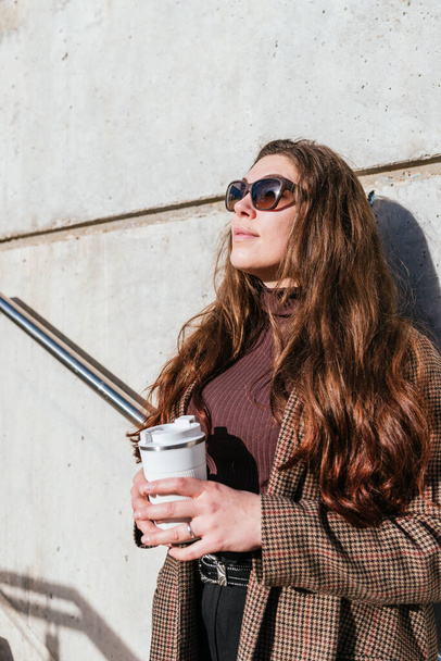 Dreamy female with takeaway coffee leaning on wall - Foto, afbeelding